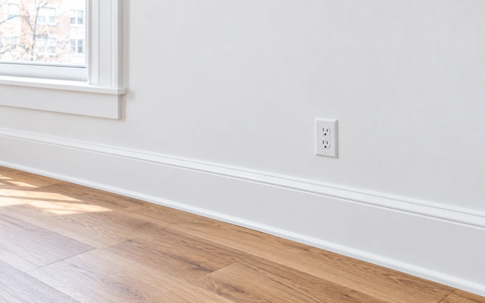 A smooth, repainted wall with new baseboard in a sunlit room